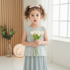 Young girl in a light blue dress holding white tulips in a bright room.